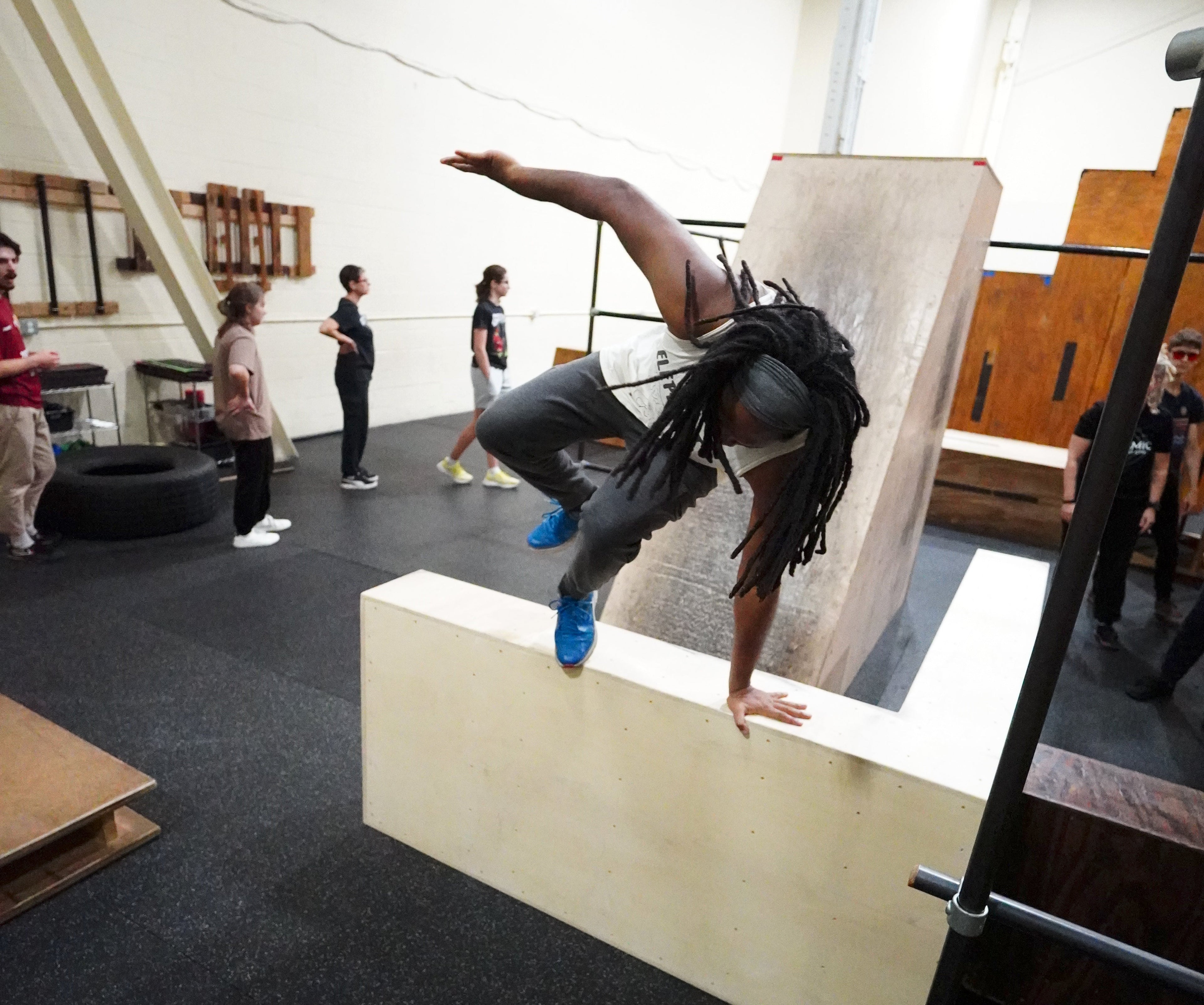 Person performing a handstand on a white box in a gym with others around